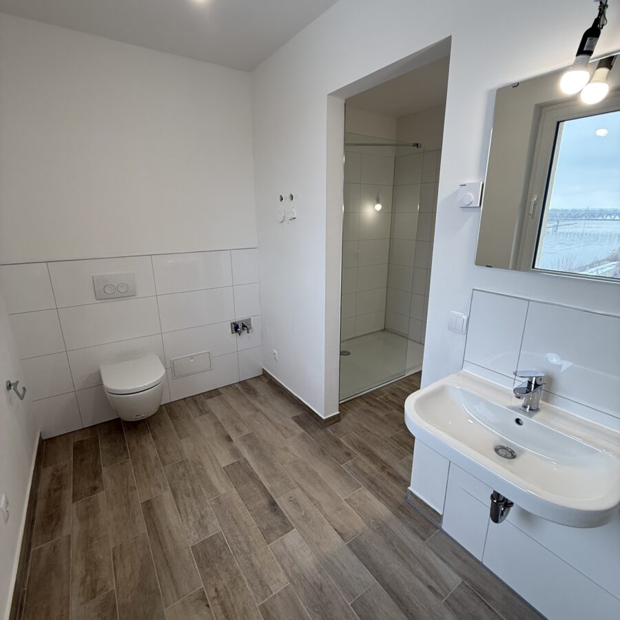 Modernes, minimalistisches Badezimmer mit Holzoptikfliesen und eleganter Dusche, strahlt Ruhe aus.