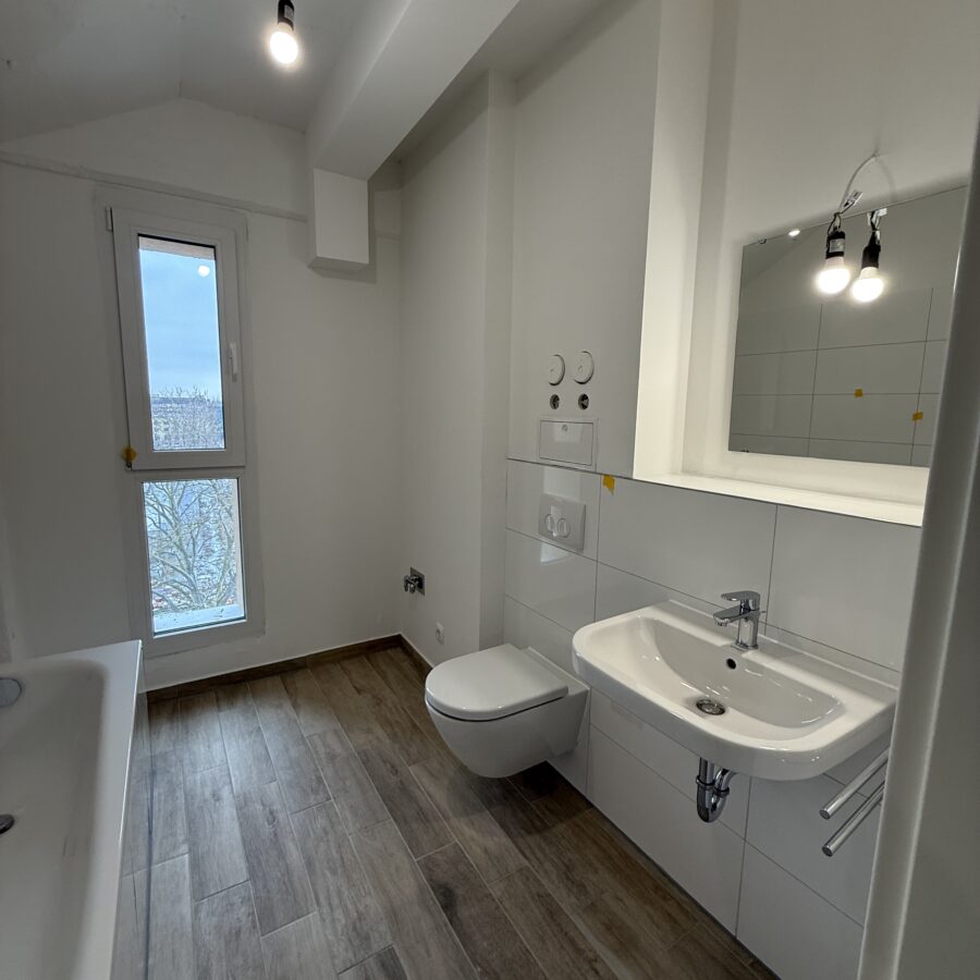 Modernes Badezimmer mit Holzfliesen, stilvollem Waschbecken, großem Fenster und minimalistischer Beleuchtung.