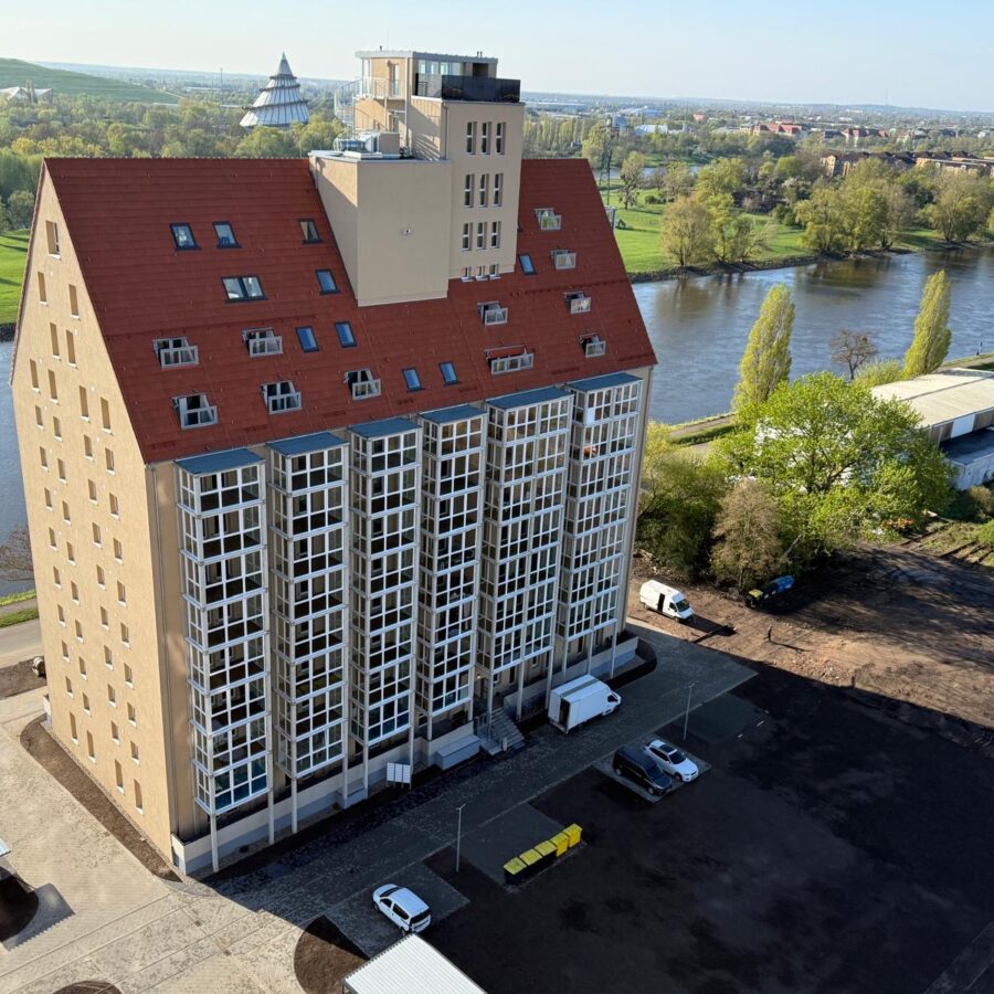 Modernes Gebäude am Fluss, umgeben von grüner Landschaft und blauem Himmel.