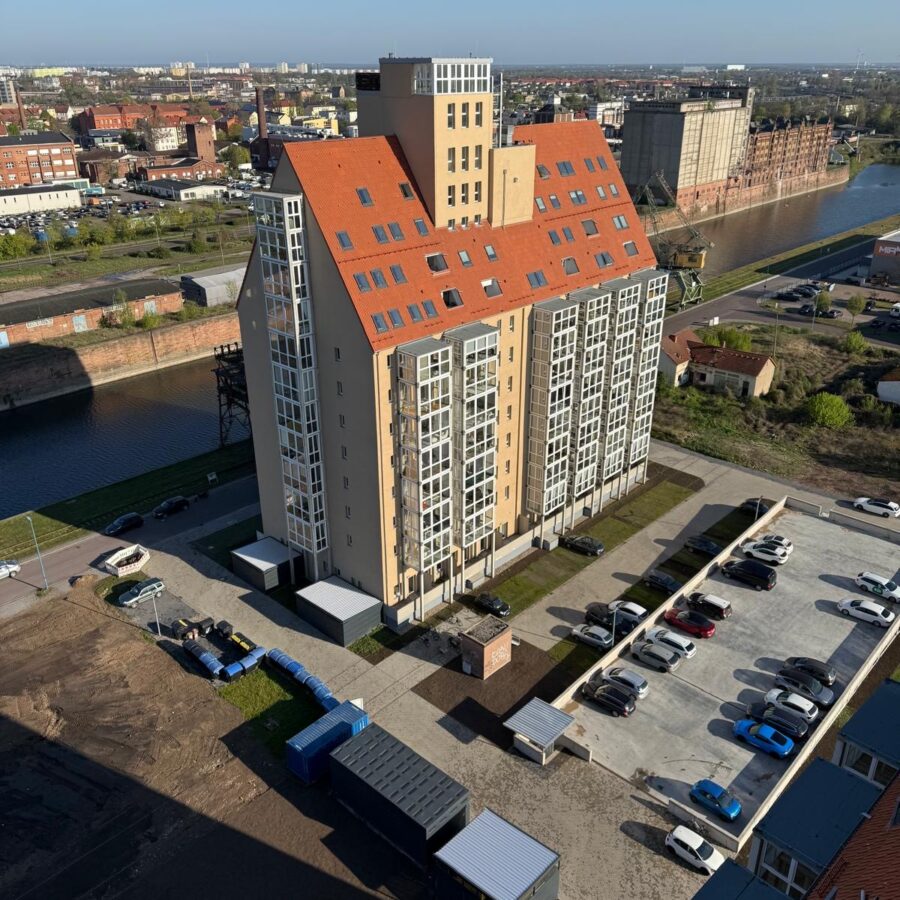 Modernes Silo B mit Hafen mit rotem Dach, umgeben von Wasser, Parkplätzen und urbaner Landschaft.