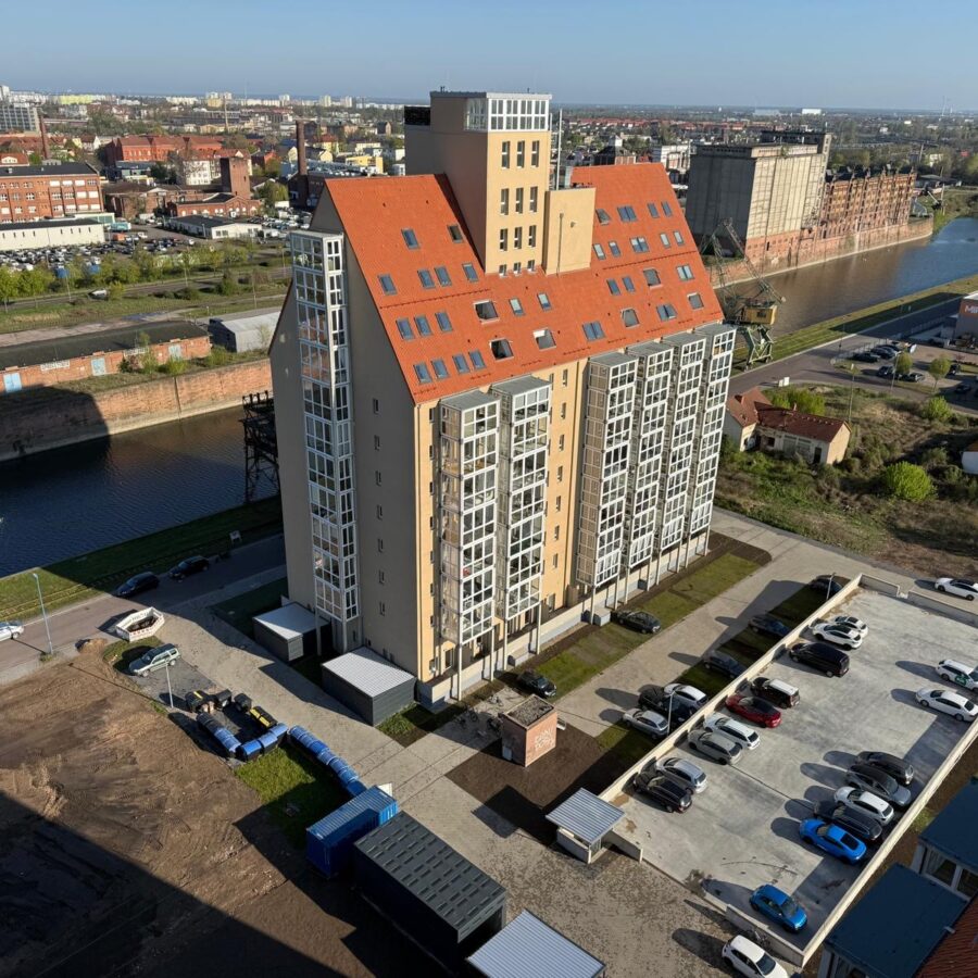 Silo B mit rotem Dach, umgeben von Wasser, Parkplätzen und urbaner Landschaft.